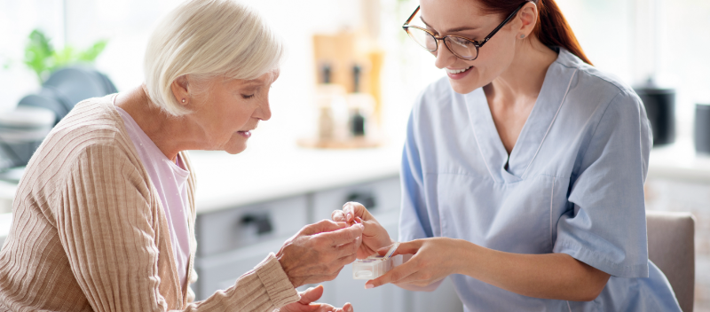 Caregiver wearing glasses giving medicine to aged lady