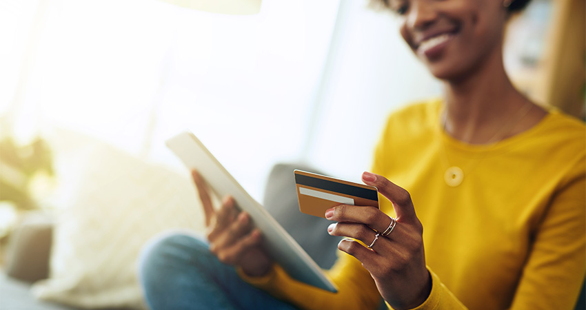 A person wearing a yellow sweater smiles while holding a credit card and a tablet, suggesting they are accepting online bill payment for healthcare services.