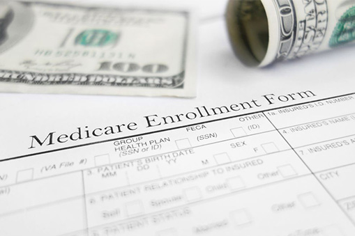 A Medicare enrollment form is shown in the foreground with part of a $100 bill, a rolled-up dollar bill, and hints of Real World Data in the background.