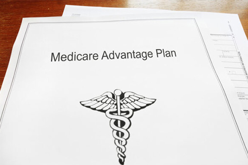 A document titled Medicare Advantage Plan with a medical caduceus symbol printed on the front, referencing Real World Data, lies atop other papers on a wooden surface.