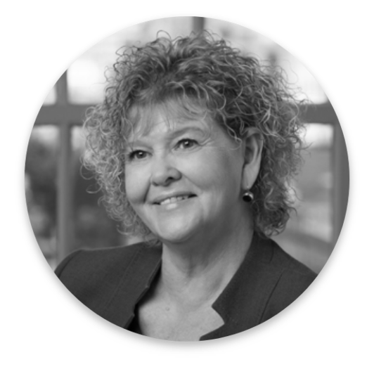 A black-and-white portrait of a smiling woman with curly hair, wearing a blazer and earrings, in front of a blurred background with window panes, reflecting her expertise in Real World Data.