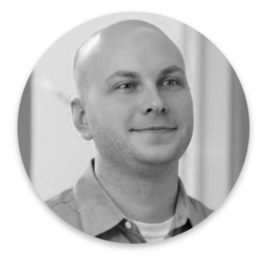 Black and white photo of a man with a shaved head, wearing a collared shirt and a slight smile, looking slightly upwards. The softly blurred indoor background lends an authentic touch, evoking the nuance of Real World Data.