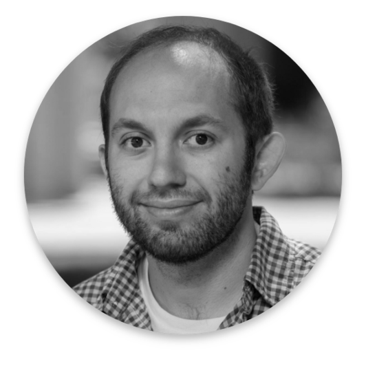 A man with short hair, a beard, and wearing a plaid shirt and t-shirt smiles slightly at the camera. The black and white image, shown in a circular frame, captures an authentic look reminiscent of real world data portraits.