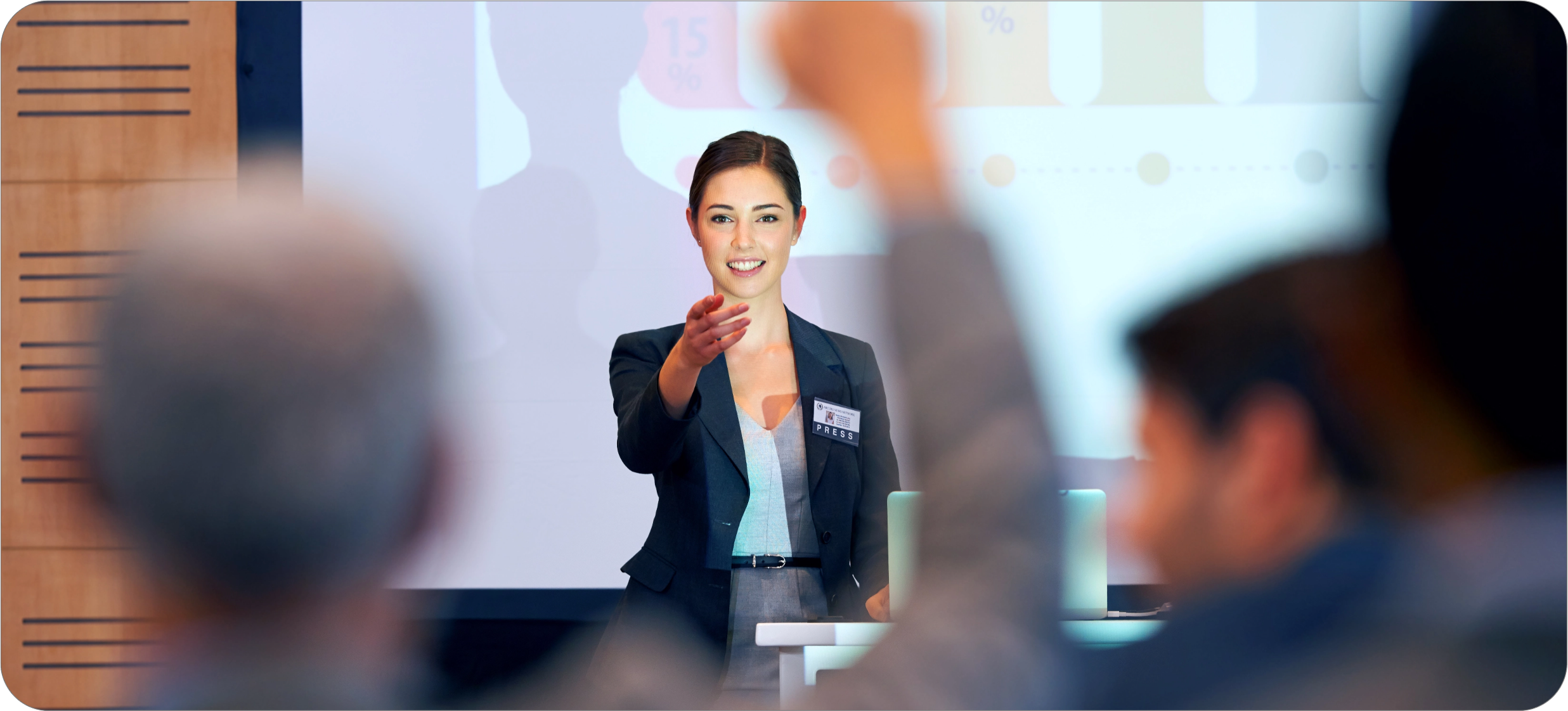 A woman in business attire stands at the front of a room, engaging with an audience. She points towards a person with a raised hand, suggesting she is addressing a question about Real World Data during her presentation.