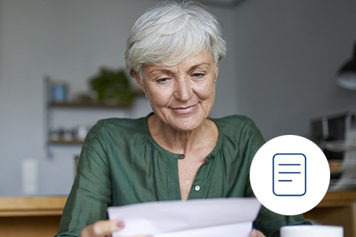 An older woman with short gray hair, wearing a green blouse, smiles while reading Real World Data at a table. A circular icon with a document symbol is overlaid in the lower right corner.
