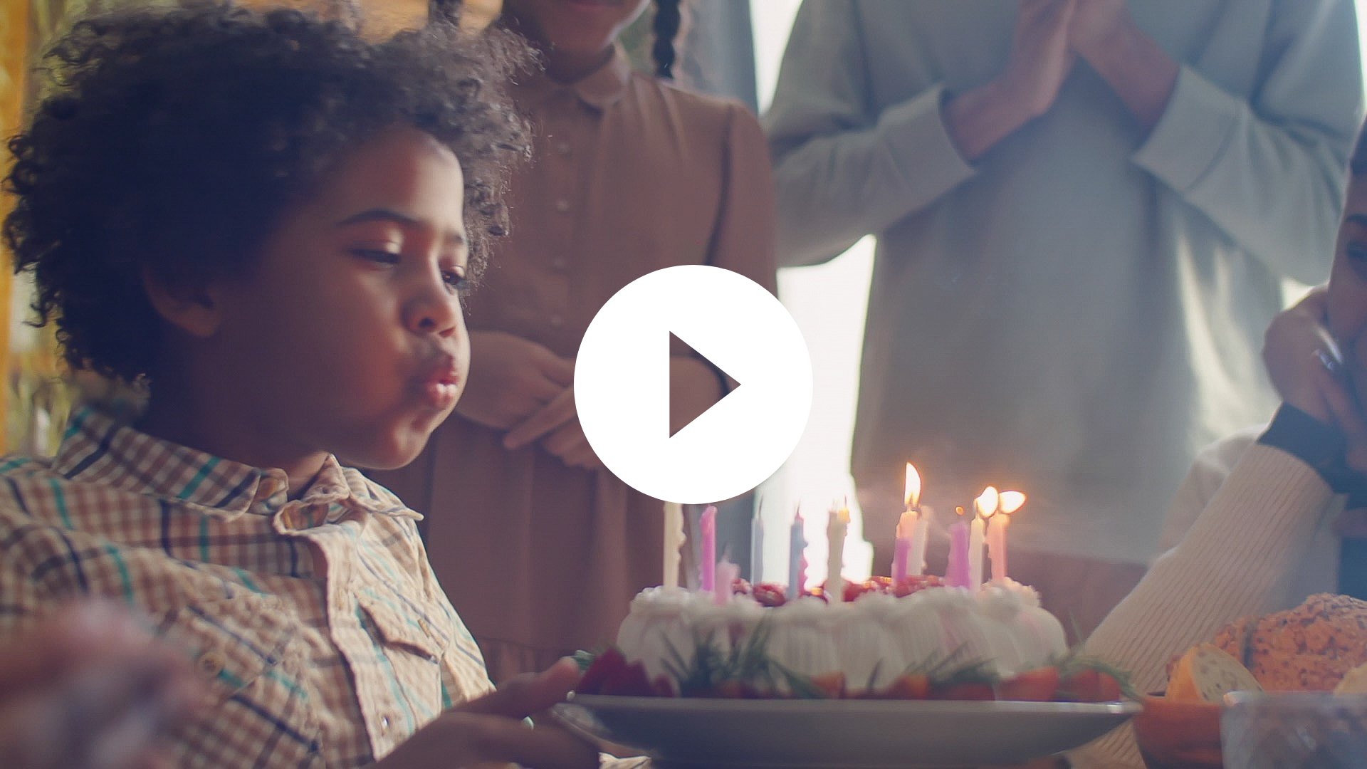 A child blows out candles on a birthday cake while people stand around, watching and celebrating.
