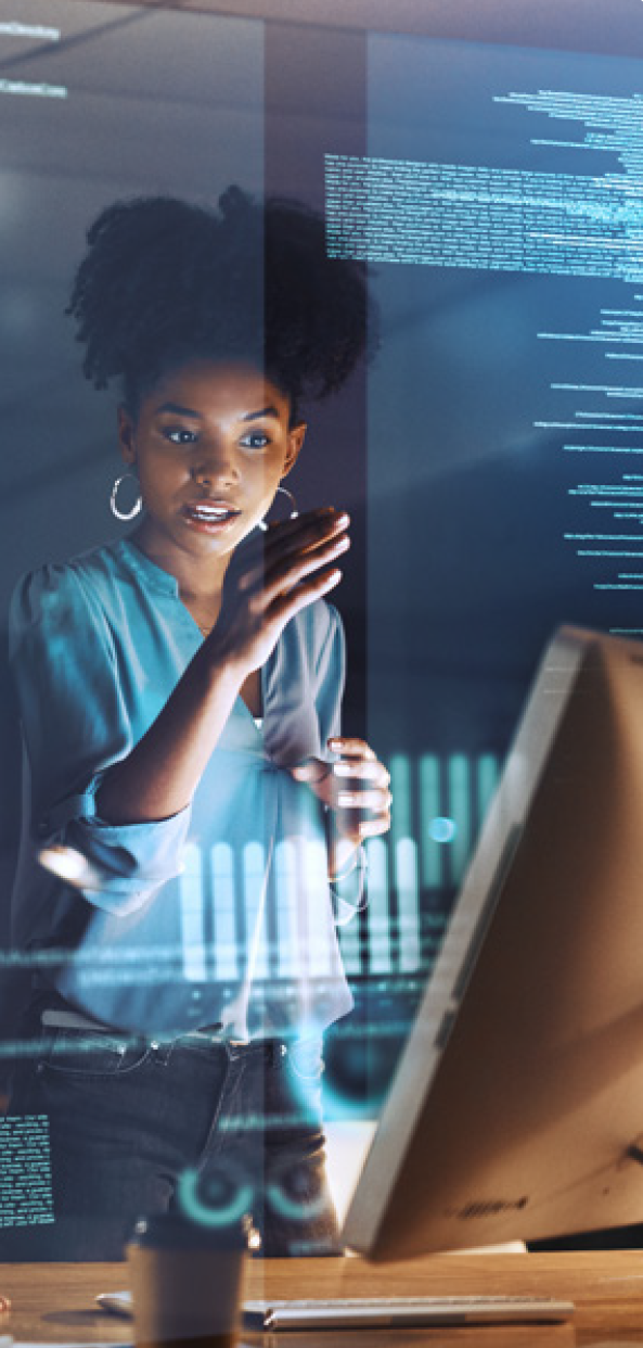 A woman in a blue blouse stands at a computer screen displaying digital code and data, appearing focused on ways to increase revenue with automation in a modern, technology-driven workspace.
