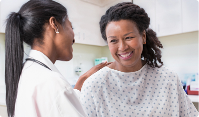 A doctor, focused on Converged Provider Enablement, gently touches the shoulder of a smiling patient in a hospital gown during a reassuring conversation in a medical exam room.
