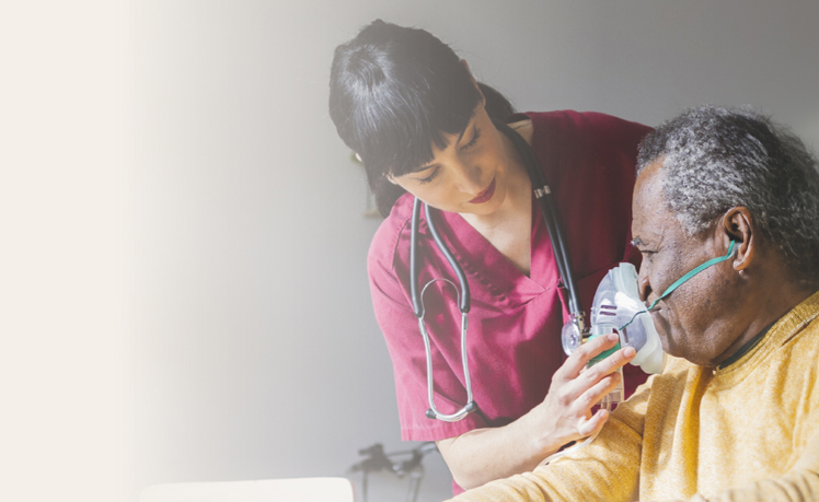 A healthcare worker in scrubs helps an older adult wearing an oxygen mask, adjusting it gently as they provide care and support, reflecting a commitment to quality improvement solutions in patient care.