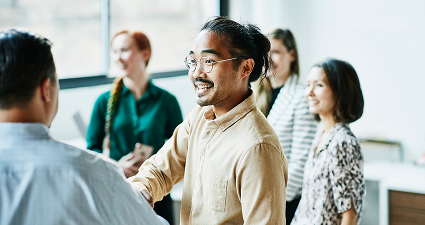 Group of healthcare professionals meeting, with image focused on one of the men with glasses shaking hands with another person