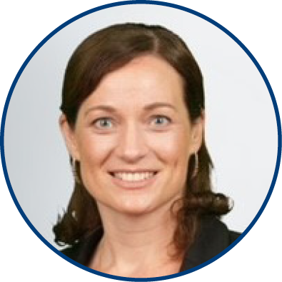 A woman with shoulder-length brown hair smiles at the camera. She is wearing a dark blazer and small hoop earrings, pictured against a plain, light background with a blue circular border around the image.