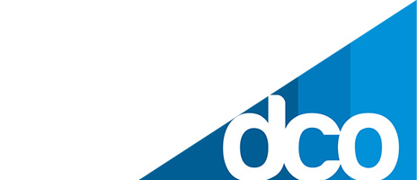 A blue and white graphic features the lowercase letters dco in bold white font, referencing a Domiciliary Care Organization (DCO), partially overlaid on a blue diagonal section with varying shades, positioned in the bottom right corner.