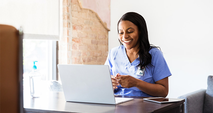 nurse in scrubs smiling while working on a laptop