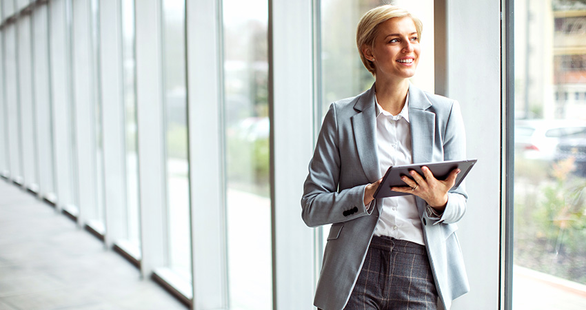 A smiling woman in a light gray suit stands by large windows, holding a tablet displaying the latest 2026 CMS Star Ratings. She looks outside, bathed in natural light, in a modern office setting.