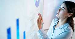 A woman in a blue shirt uses a stylus to interact with graphs and charts displaying quality measure performance by payer type 2024 on a large touchscreen.