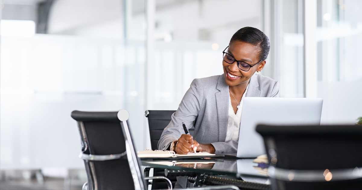 Woman smiling and writing in a notebook in front of computer