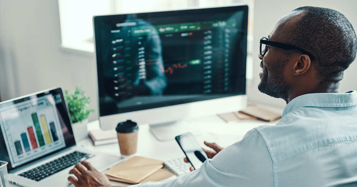 Person at desk looking at laptop and monitor with analytics on screen