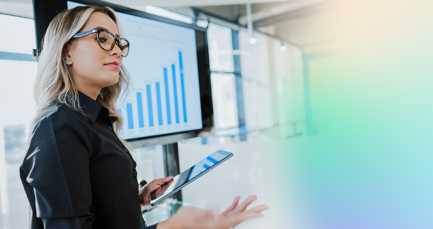 A woman holding a tablet presents data on a screen displaying a rising bar graph in a bright, modern office setting, illustrating how The Clover Decision changed more than one plan’s Star Rating.