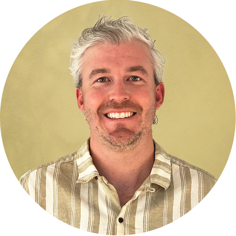 Man with grey hair and beard smiling for his headshot