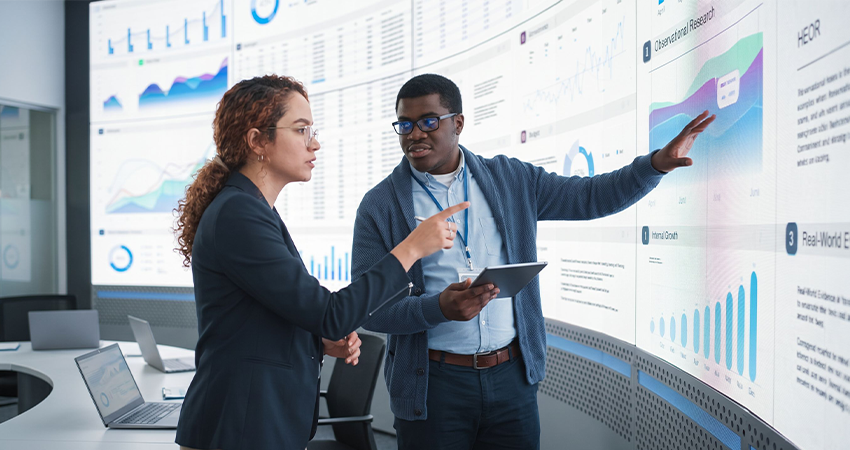 a man and woman working together discussing data on a very large screen